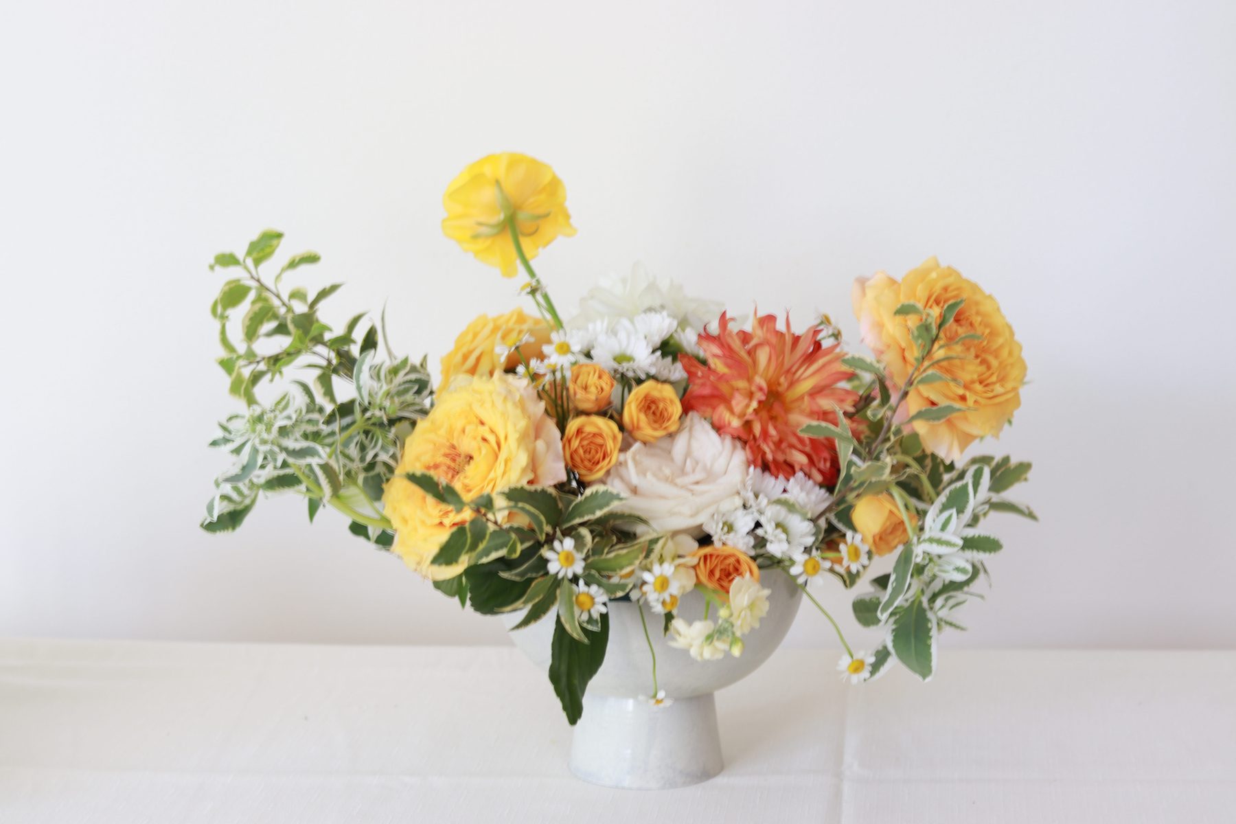 Amber-toned arrangement of roses and dahlias in a stone pedestal compote