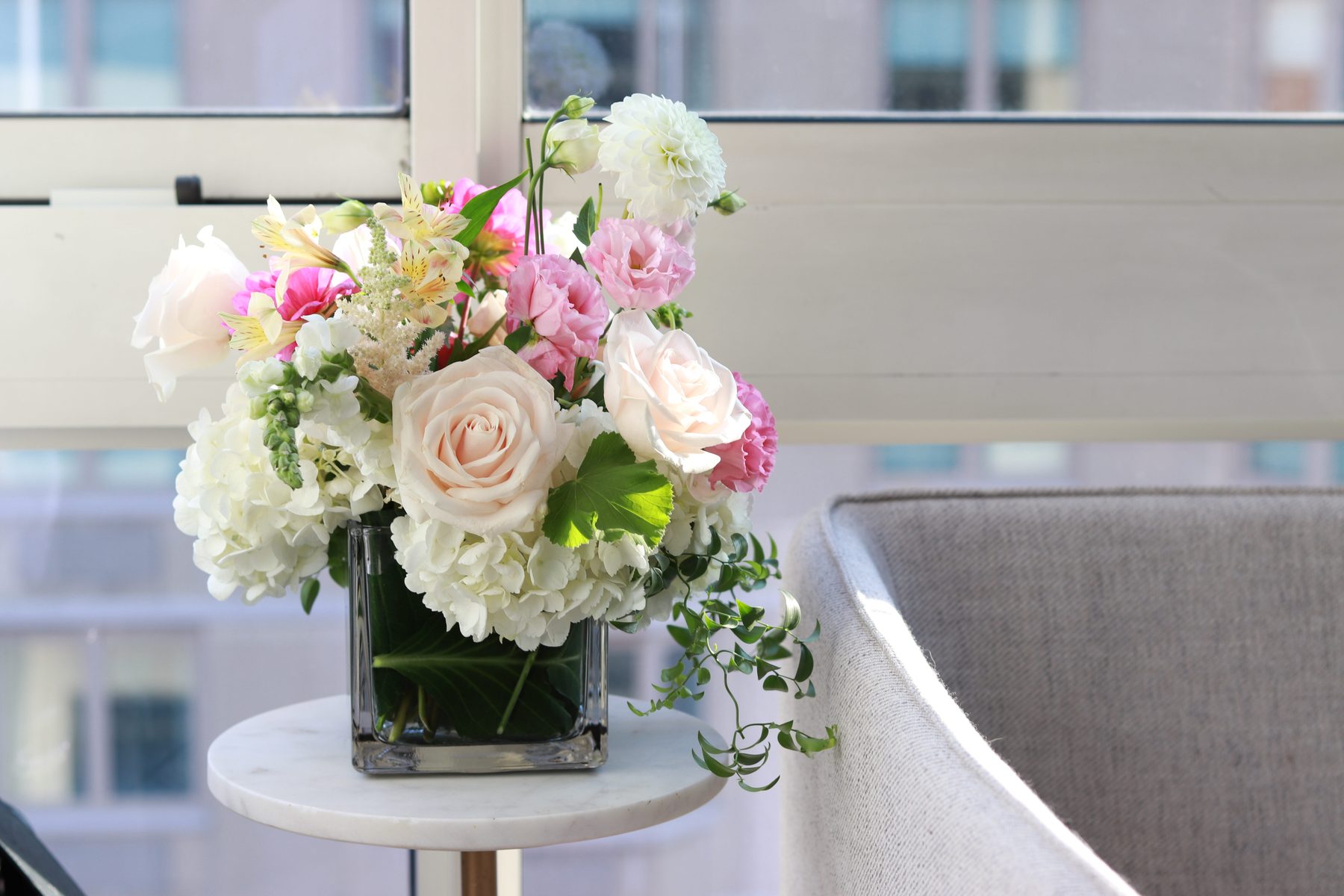 Blush rose and hydrangea arrangement in a glass vase by a window