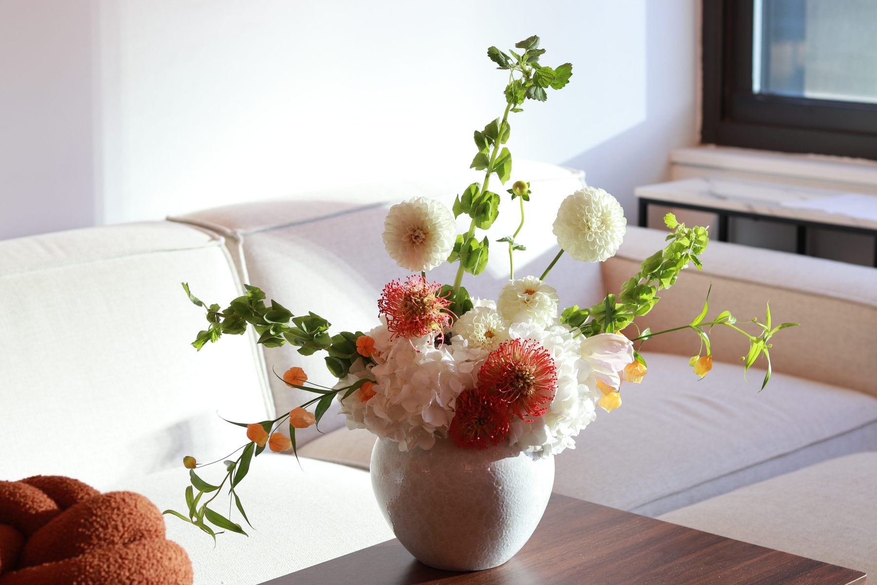 White dahlia, hydrangea, and pincushion protea arrangement in a white vase on a coffee table