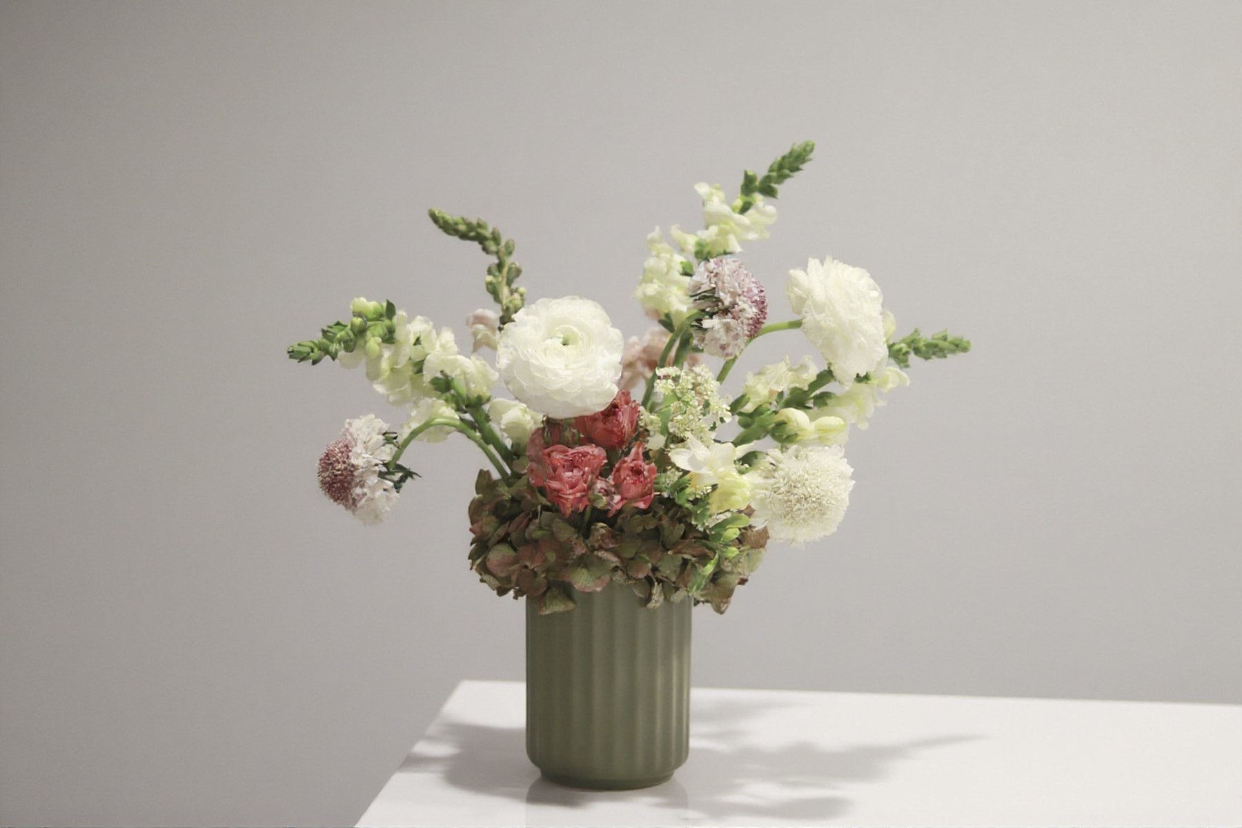 Ranunculus, snapdragon, and hydrangea arrangement in a ribbed green vase