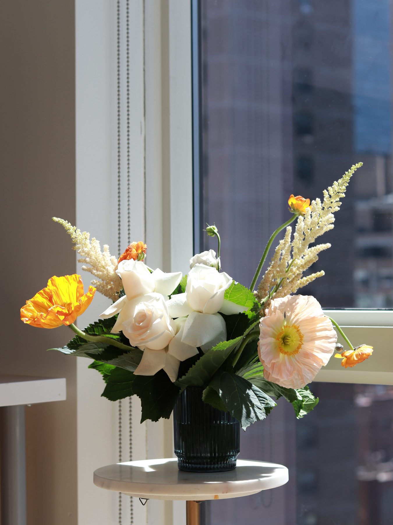 Ivory rose and peach poppy arrangement by a city window, alternate angle