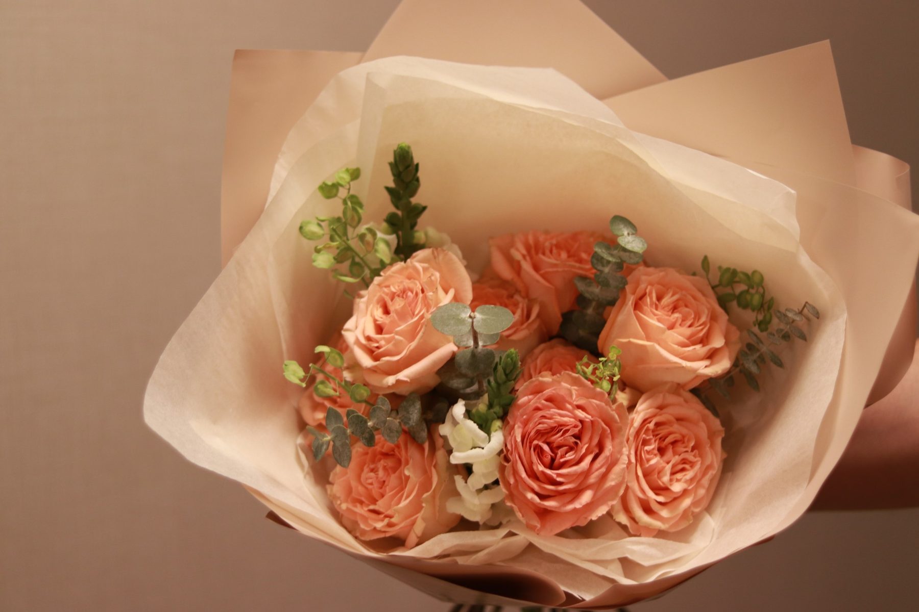 Peach garden roses with eucalyptus and white snapdragon, hand-wrapped in blush paper