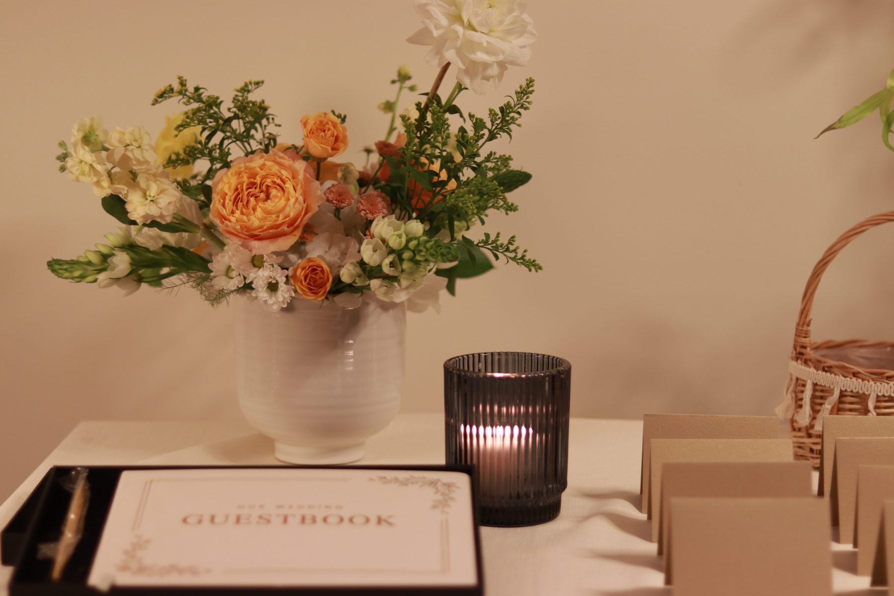 Peach garden rose arrangement styled beside a wedding guestbook and escort cards