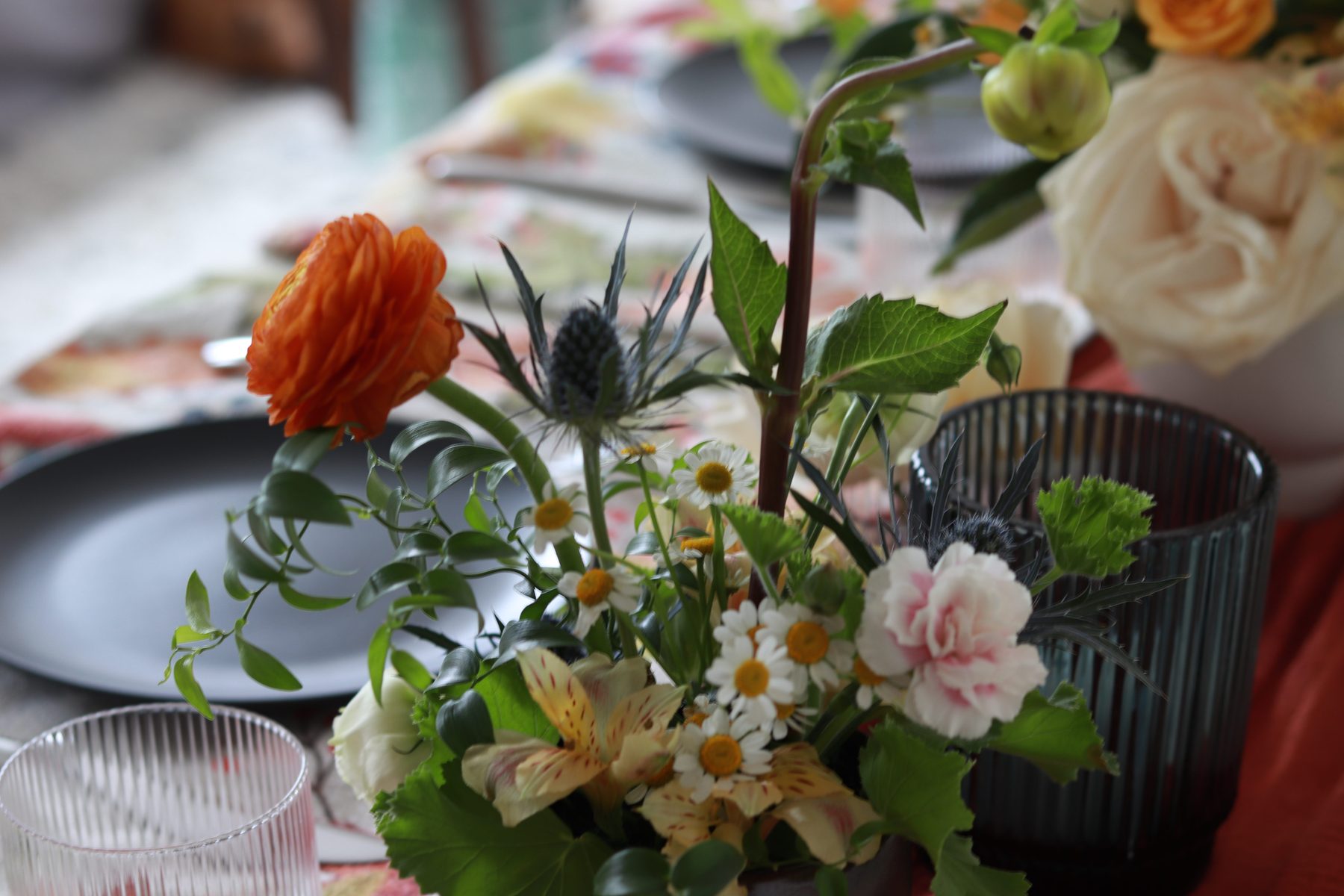 Sea holly, ranunculus, and daisy centerpiece detail on a set dining table