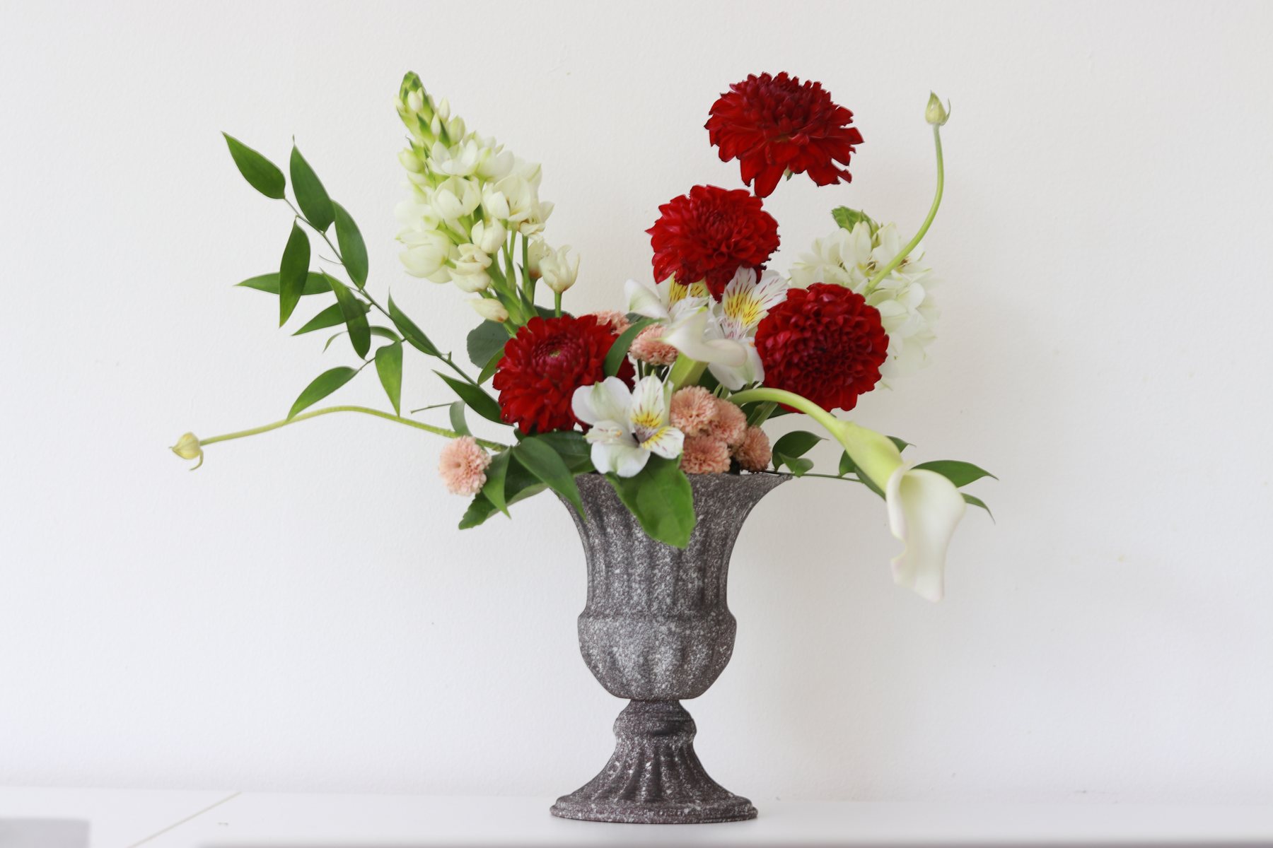 Red dahlia, white alstroemeria, and calla lily arrangement in a grey stone urn