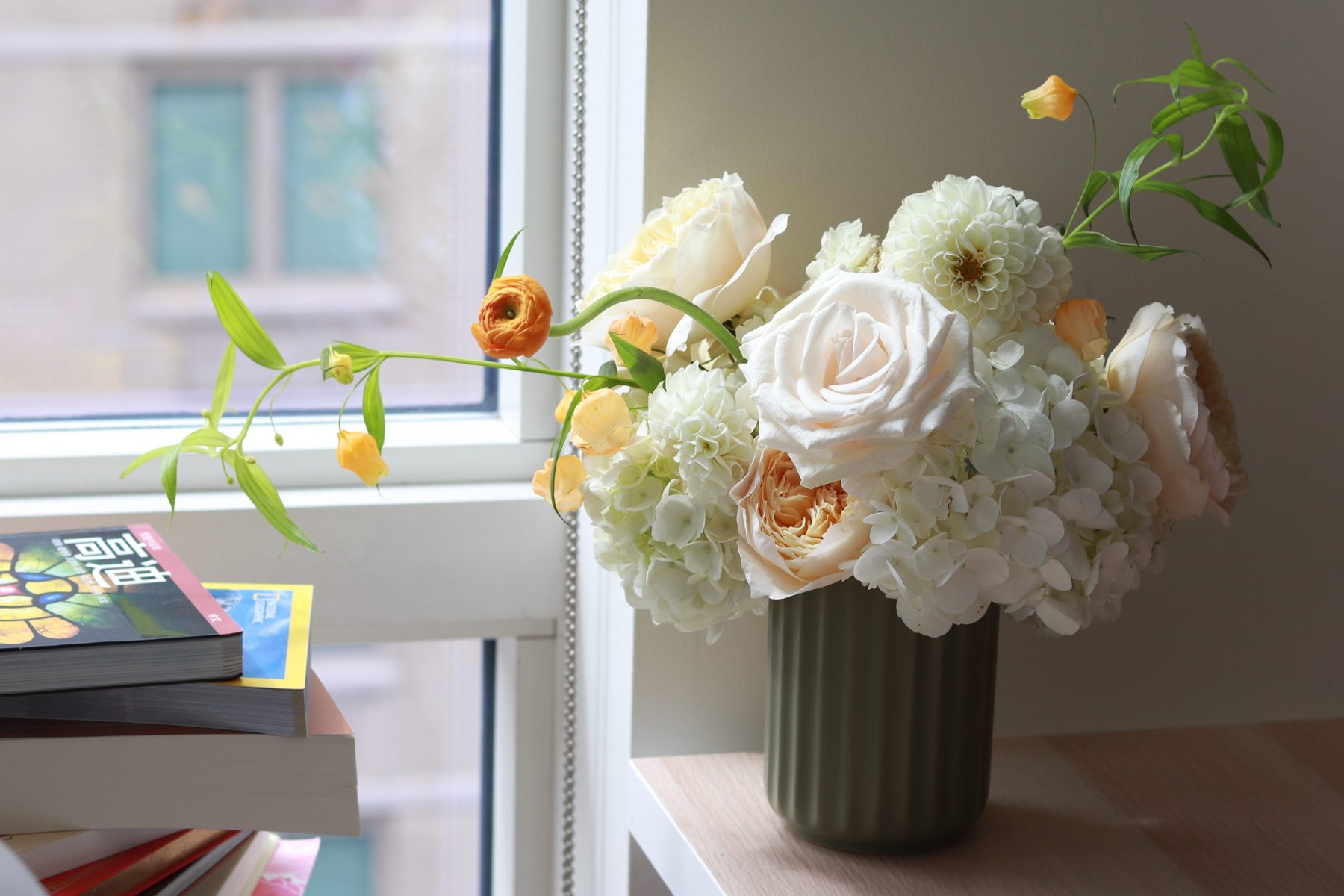 Ivory rose, hydrangea, and orange ranunculus arrangement in a sage green vase