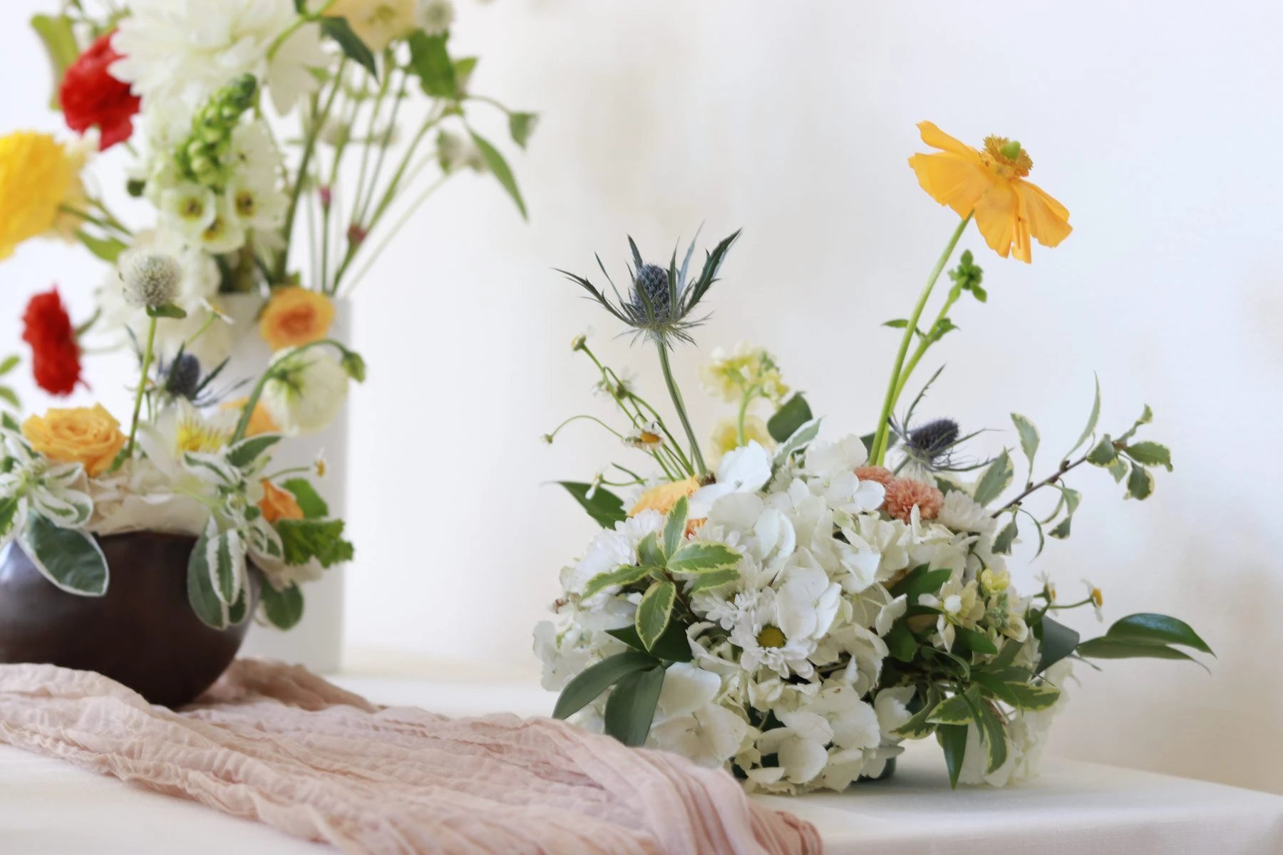 Petite arrangement of white hydrangea, sea holly, and a yellow poppy on a table with a blush runner