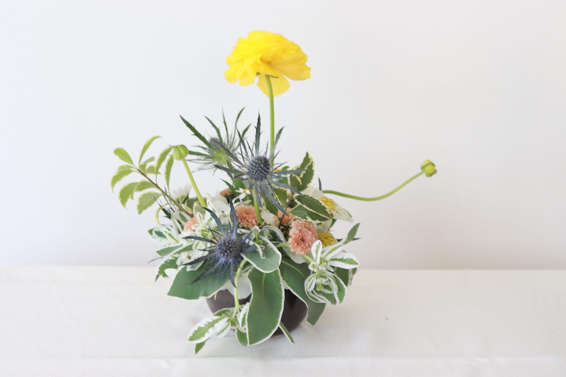 Sculptural sea holly and yellow ranunculus arrangement