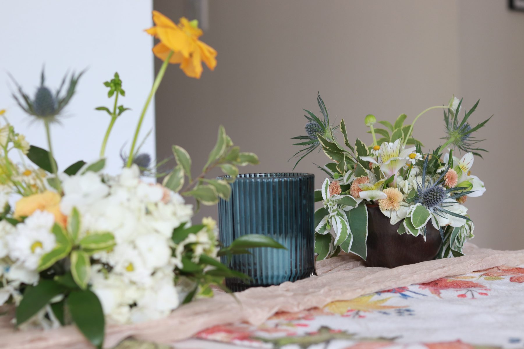 Sea holly and ranunculus arrangement detail beside a votive candle