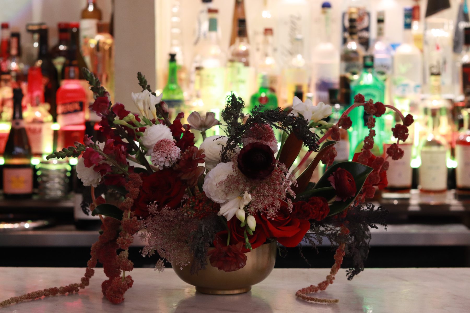 Burgundy and blush arrangement in a brass bowl on a marble bar