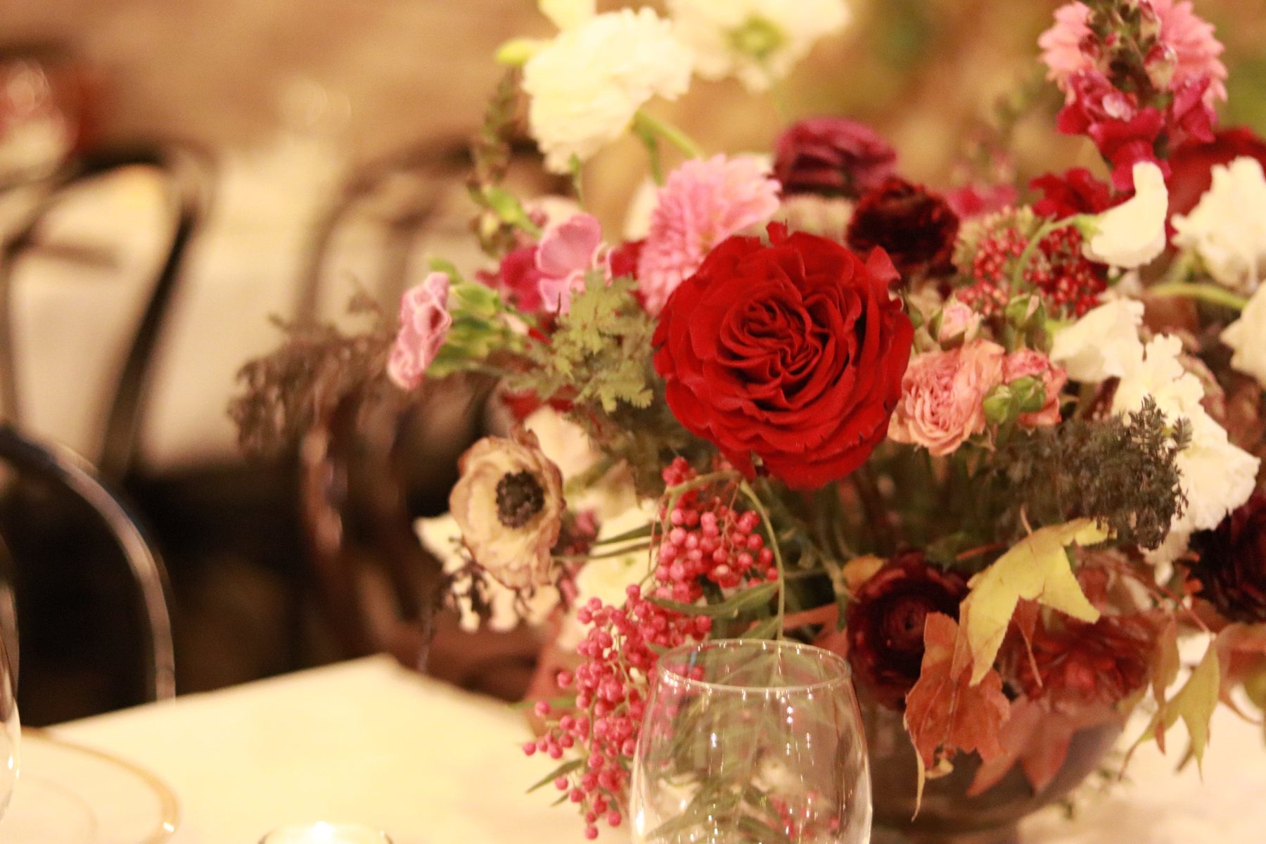Close view of a red rose centerpiece with pink berries and autumn leaves