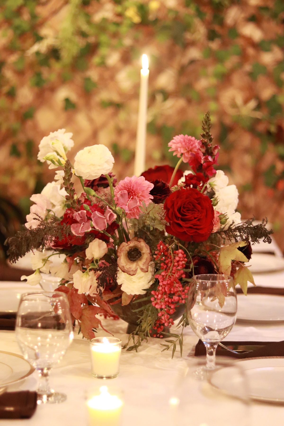 Burgundy rose and dahlia centerpiece beside a taper candle at a private dinner