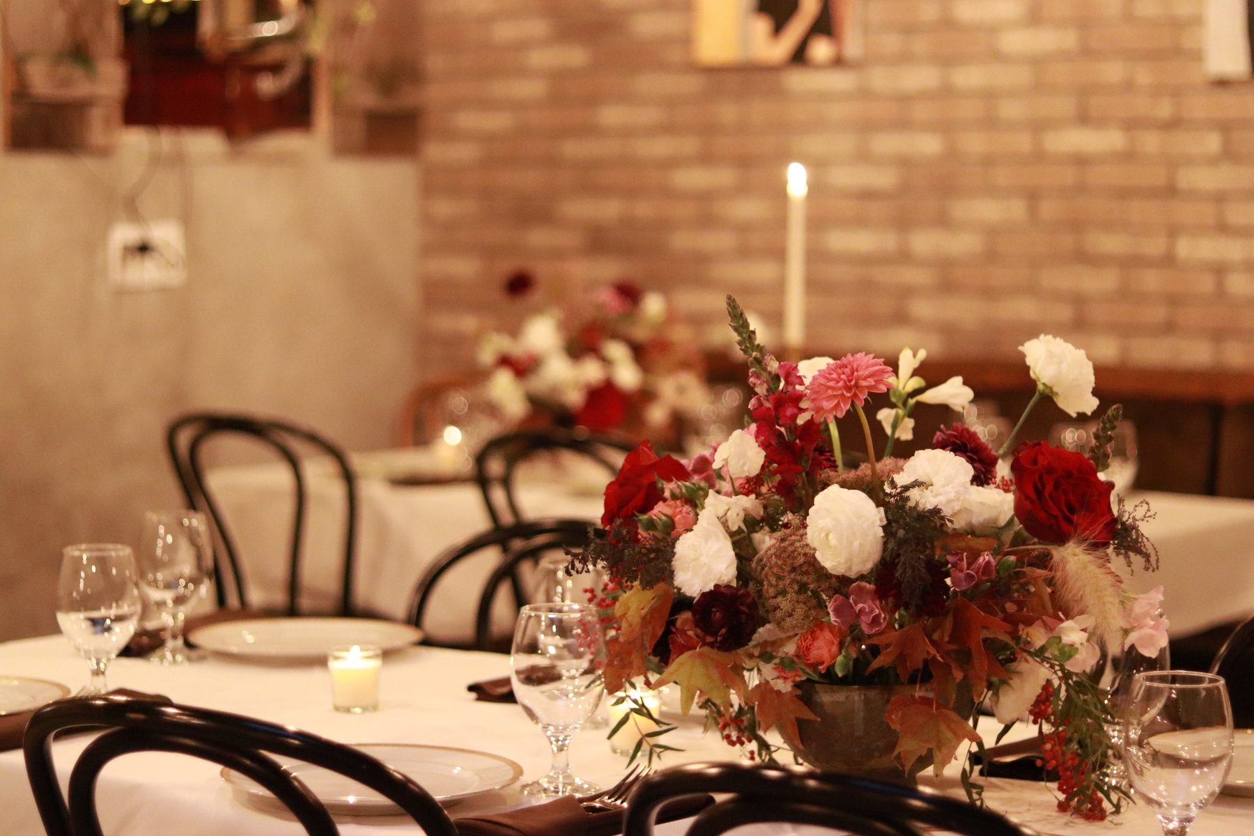 Burgundy centerpiece and a taper candle on a dinner table against a brick wall