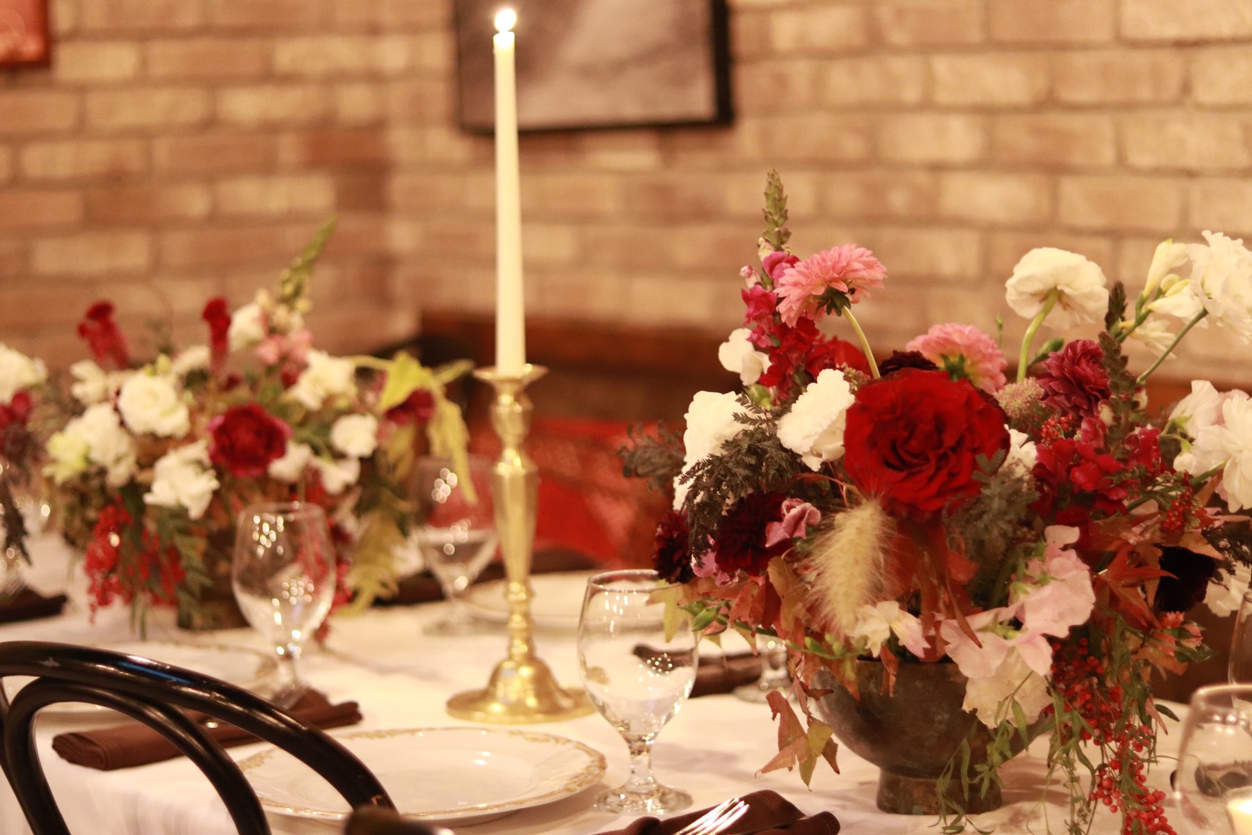 Two burgundy and blush centerpieces with a taper candle on a set dinner table