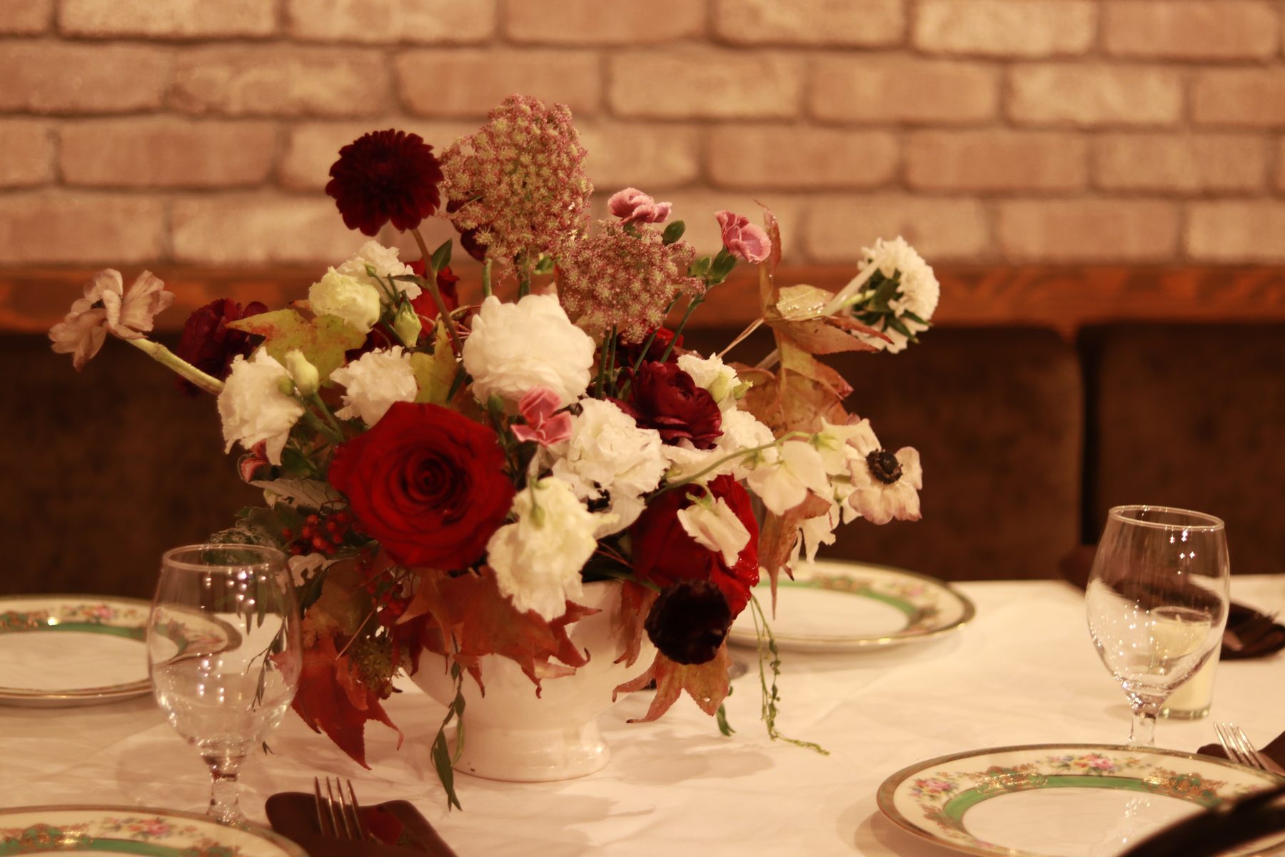 Burgundy and blush centerpiece on a private dinner table against a brick wall