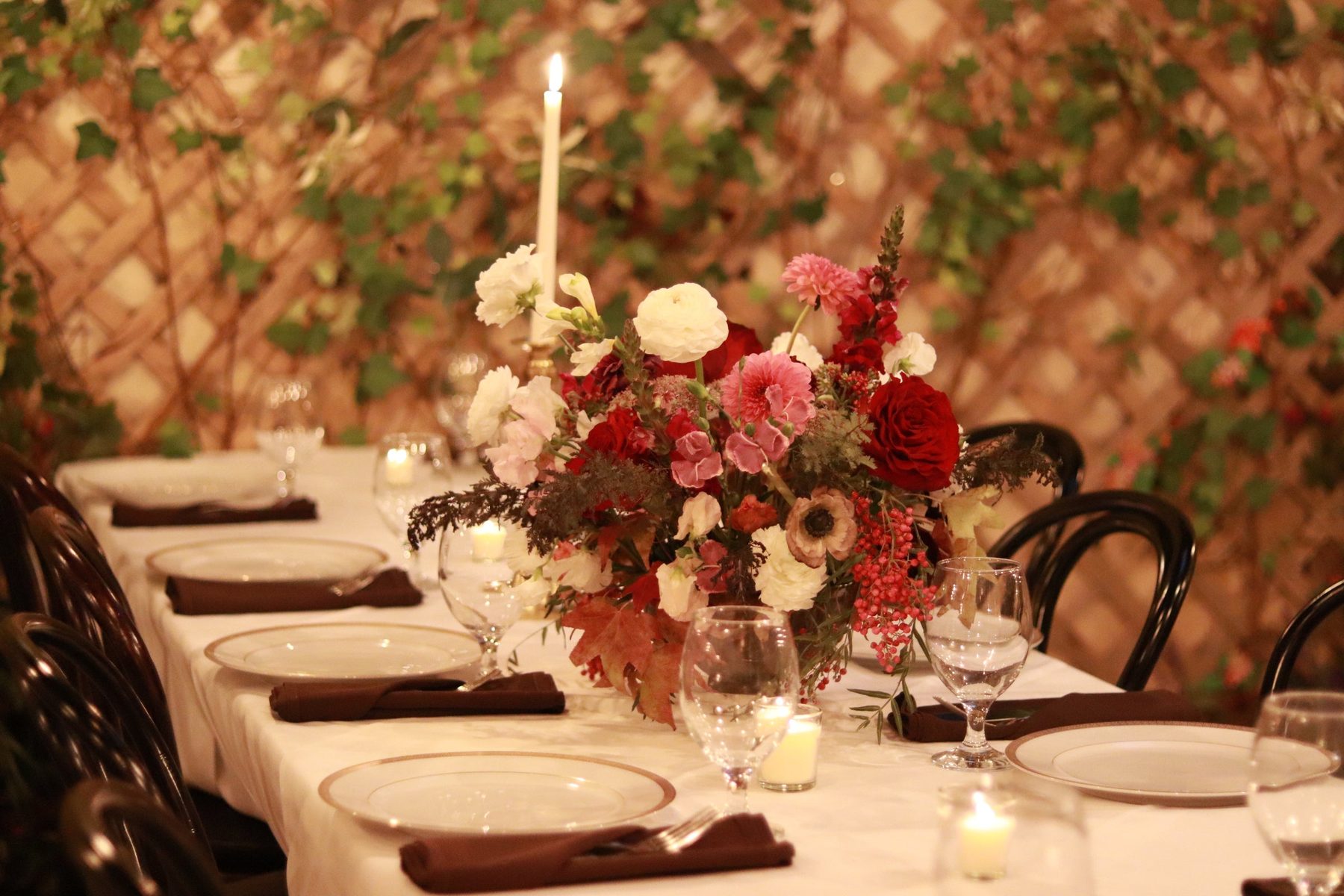 Burgundy and blush centerpiece on a long dinner table in front of an ivy trellis