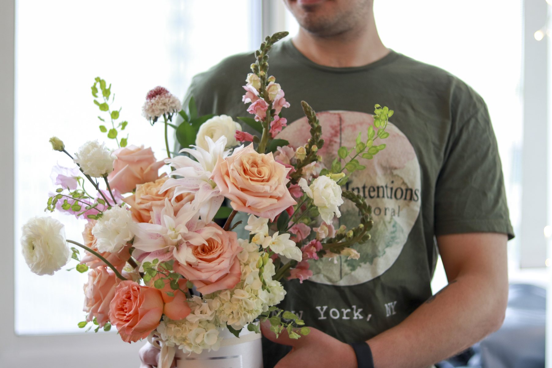 Peach and blush flower box arrangement held up in a bright room