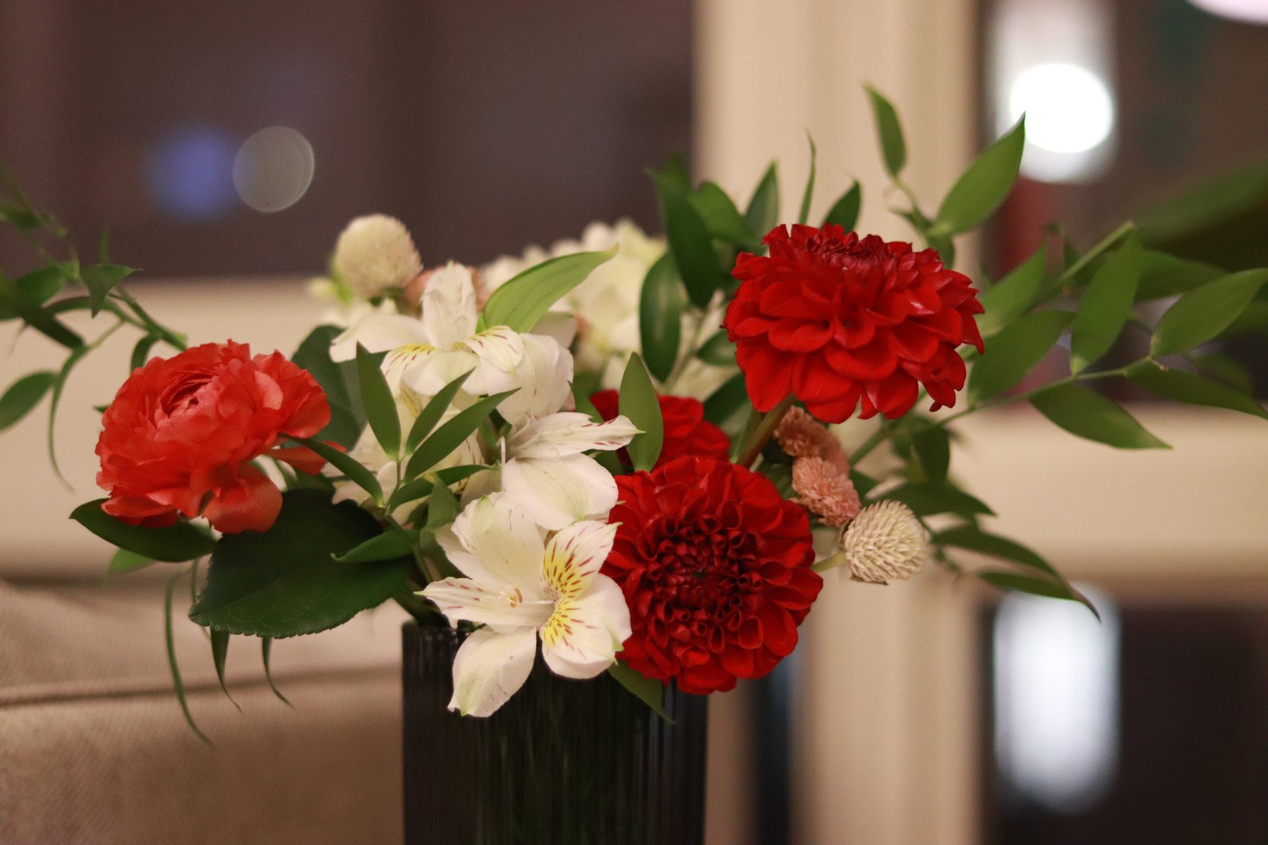 Red dahlia, ranunculus, and white alstroemeria in a dark ribbed vase